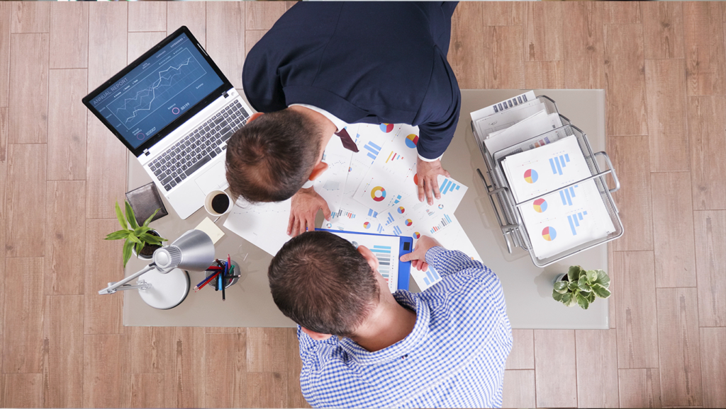 Overhead view of professionals collaborating on business analysis using data charts and a laptop.